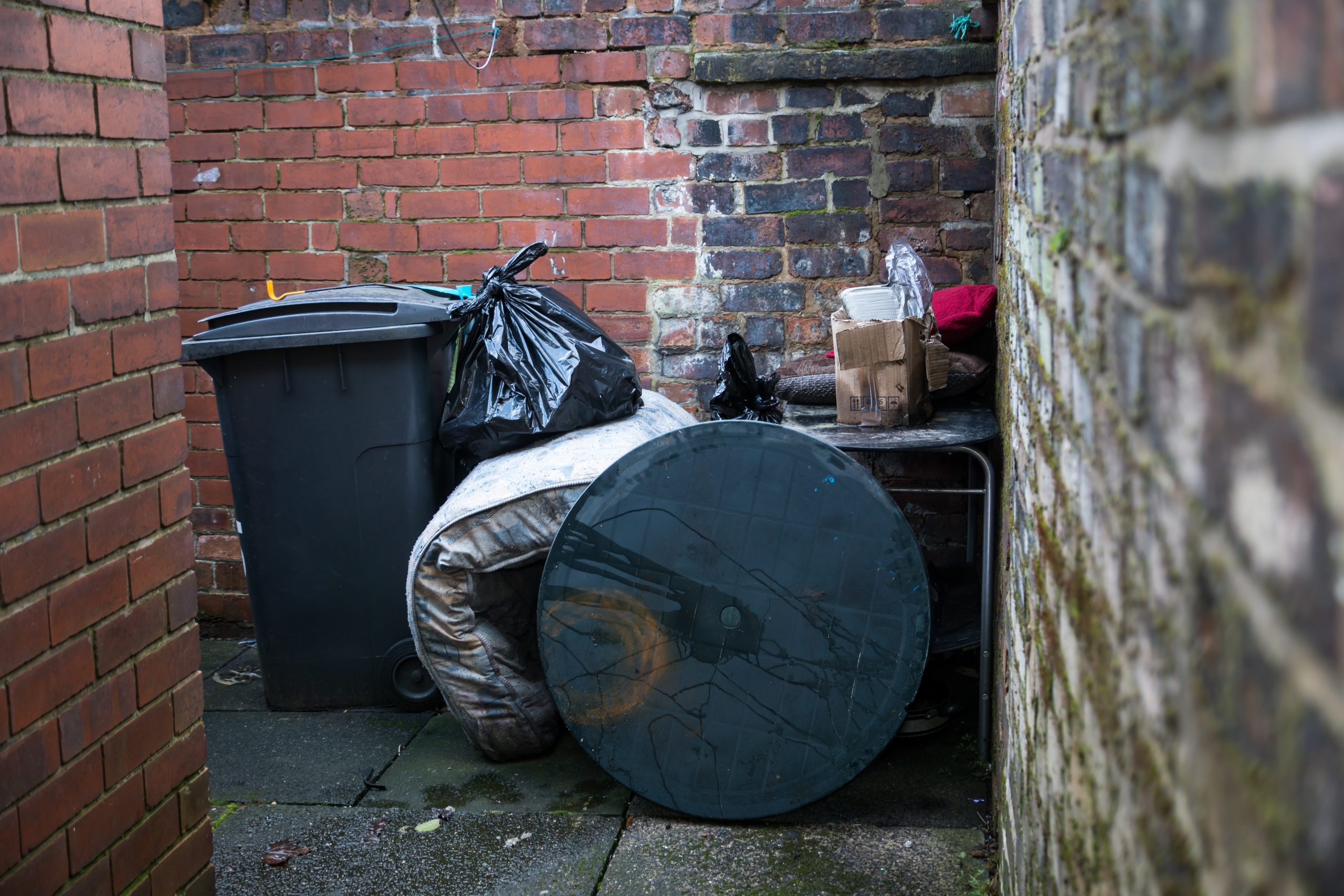 A trash can with a black lid sitting in a brick wall.