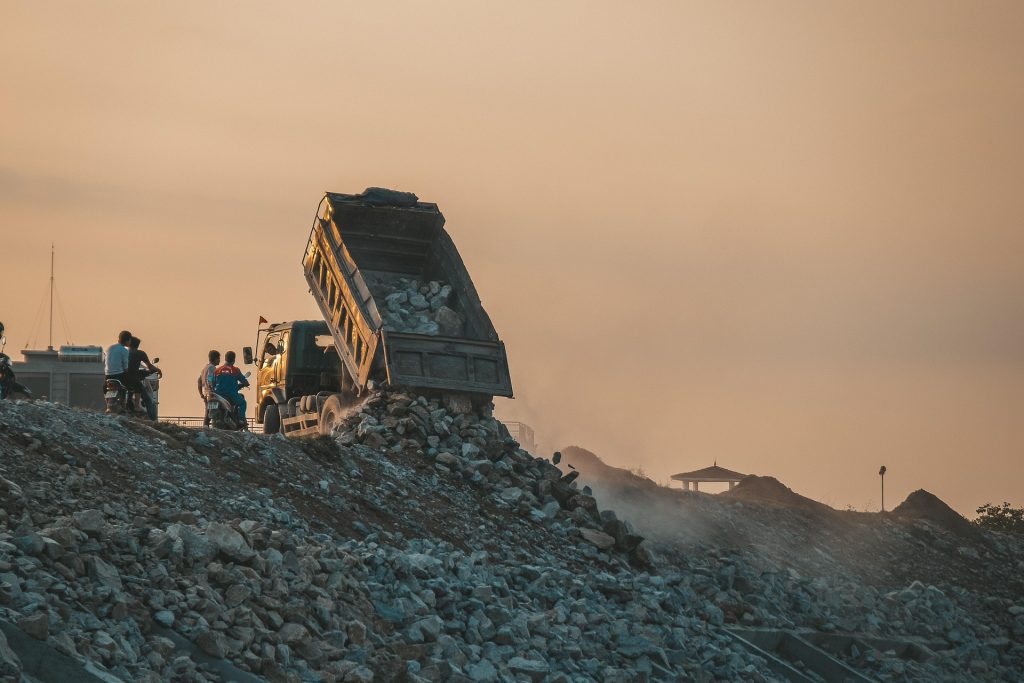 A dump truck is working on a pile of rocks at sunset.