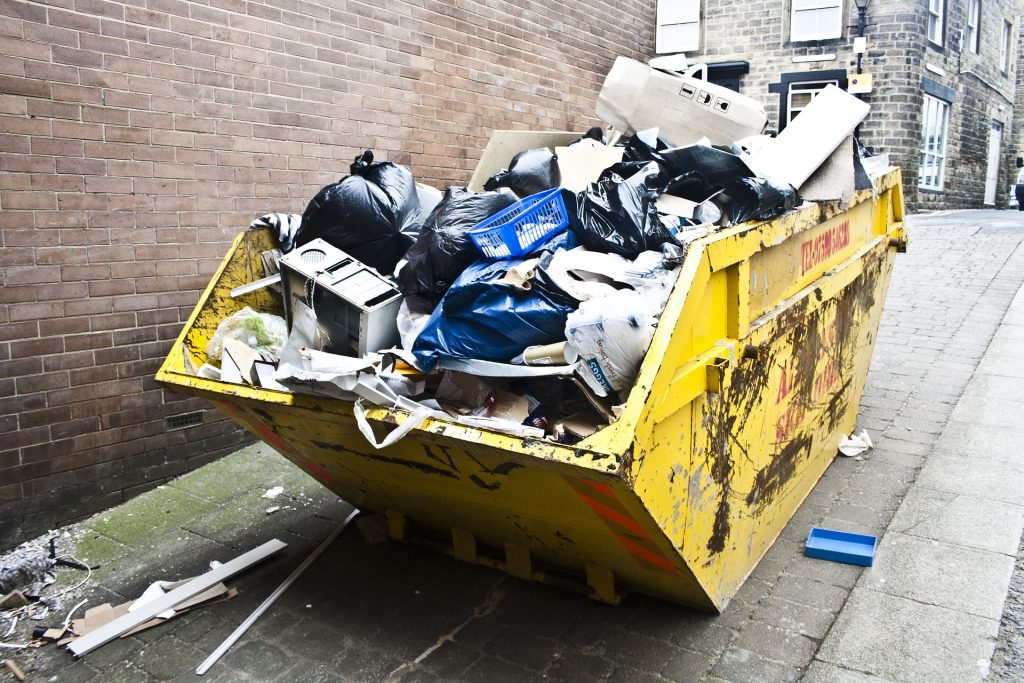 A yellow garbage bin sits on the side of a street.