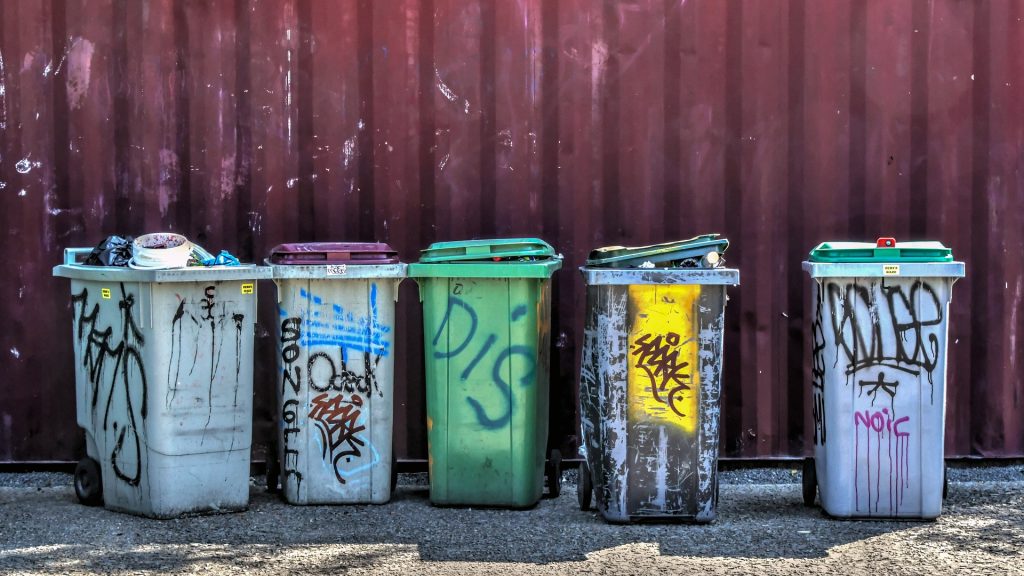 Row of graffiti-covered recycling bins for various materials, showcasing the organized waste collection services.