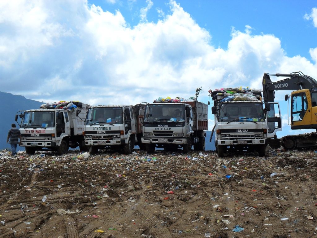 A group of garbage trucks parked in a dirt field.