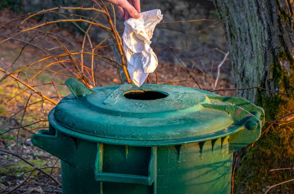 A person throwing a paper into a green rubbish can