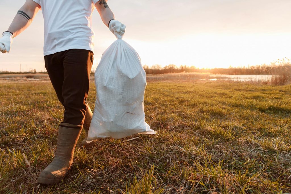 A man in a field with a bag of rubbish