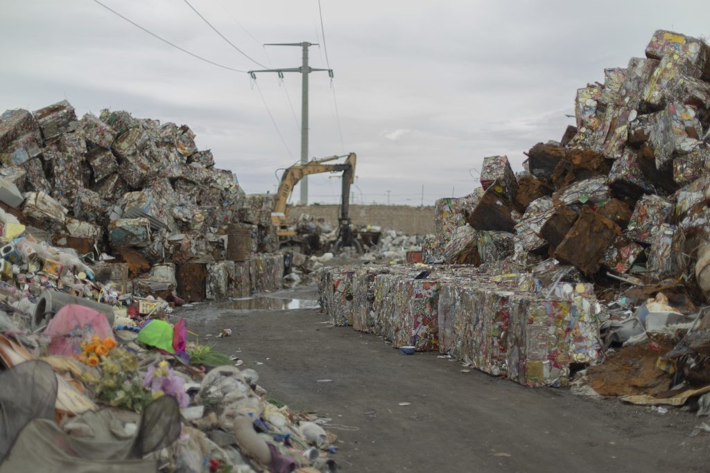 Stacks of compacted recyclable materials with an excavator in the background, managed by Senior Waste Removals.